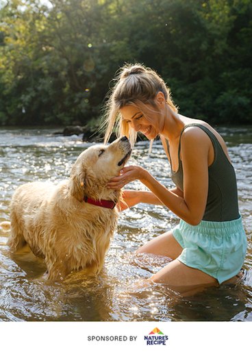 A woman is petting her dog on a sunny day in a lake. 