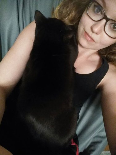 black cat blends into woman's black tank top