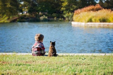 Cat and child sitting by a lake.
