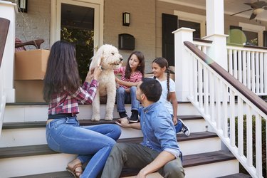 Family With Dog Sitting On Steps Of New Home On Moving In Day