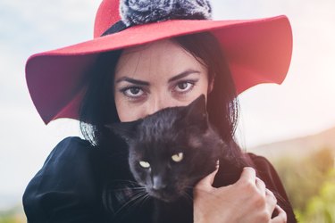 Young beautiful glamorous black-haired woman holding black cat