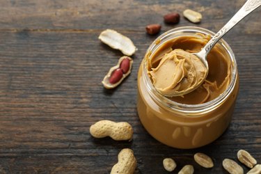 peanut butter in an open jar and peanuts