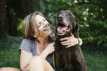 Smiling woman sitting on grass with Labrador Retriever