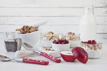 Ready-made healthy breakfast - muesli or granola with pomegranate, chia seeds and fresh natural yoghurt on white rustic wooden background, close-up, selective focus, shallow depth of field