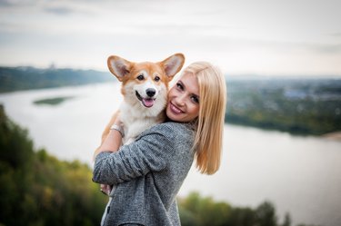 young woman smiling at camera holding corgi dog
