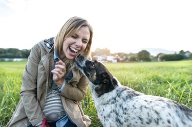 Pregnant person with dog in a green field.