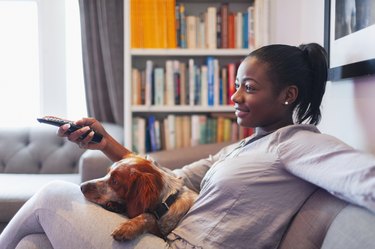 Young woman and dog relaxing, watching TV on living room sofa