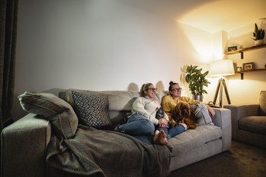 Couple watching TV on sofa with their dog.