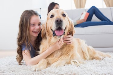 Girl embracing Golden Retriever while lying on rug