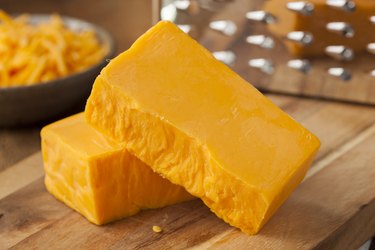 Organic Sharp Cheddar Cheese block with grater in background