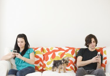 Man and woman dialing cell phones on opposite ends of sofa