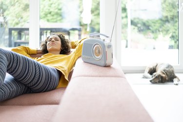 Woman lying on couch listening to music with portable radio at home