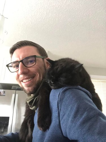 Man with black cat sleeping on his shoulder