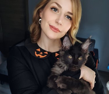 women in halloween sweater holds black cat