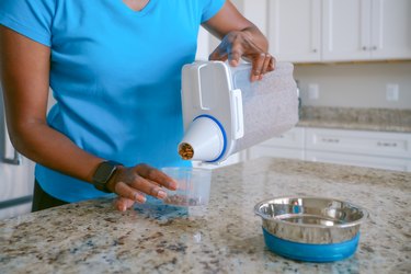 Woman pouring dry pet food into a container.