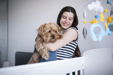Happy young mom and family dog looking baby in crib.