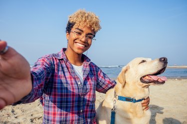 African American woman hugging her dog while taking a selfie at the beach