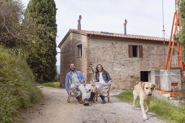 Happy mature couple sitting on chair with dog in front of house