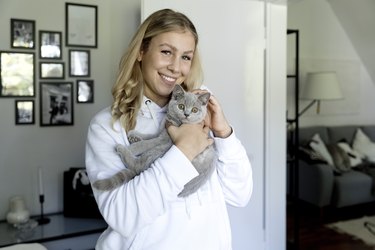 Smiling young woman holding gray cat at home