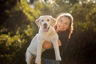 Young woman holding her dog up , looking at camera and smiling