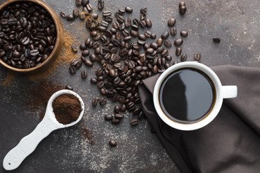 A cup of coffee, coffee beans, and ground coffee