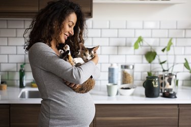 Happy pregnant woman carrying cat in kitchen