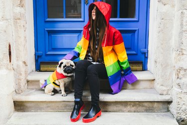 Happy young woman and her dog in rainbow coats walking in the sunny old city center enjoying the springtime