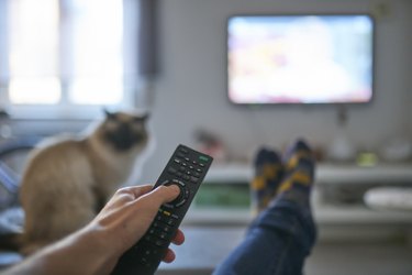 Hand of man pointing remote control at working television screen