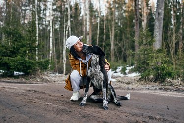 Portrait of a woman in a yellow jacket walking through the woods with a dog in cool weather