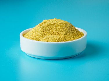 Nutritional yeast in white bowl on blue background.
