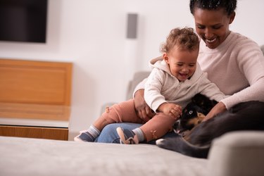 Mother and baby playing with their dog at home.