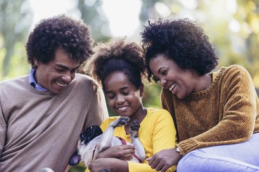 Beautiful young family lying on a picnic blanket with their dog, enjoying an autumn day in park