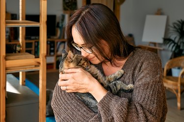 Middle-aged woman hugging cute tabby cat in indoor scene. Human-animal relationships. Funny home pet. Homeless pets.