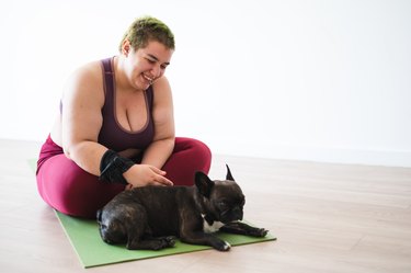 woman smiling and petting her dog on yoga matt
