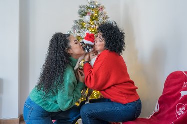 Mother and daughter kissing their cat in front of christmas tree.