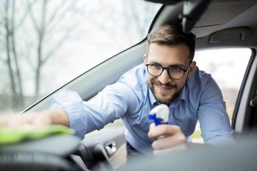 Smiling young man cleaning the interior of a car with a piece of cloth