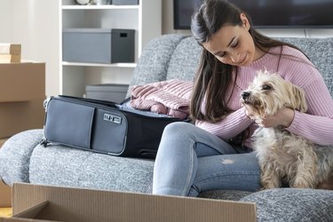 A girl sitting on a couch with a small dog and a suitcase