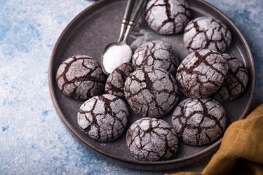 Several chocolate crinkle cookies, dusted with powdered sugar, in a bowl.