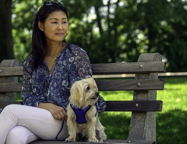 Woman sits on bench with champagne maltipoo on a clear day