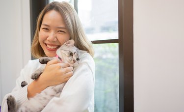 Young woman smiles and holds cat in living room