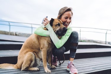 Happy woman with smartphone hugging dog