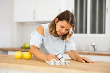 Positive woman cleaning kitchen table at home