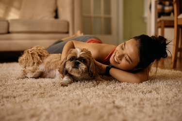 Happy Asian woman and her dog lying down on the carpet at home.