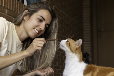 Young woman smiling while educating her cat pet with a treat in the front patio