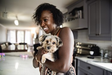 Woman holding puppy dog in kitchen.