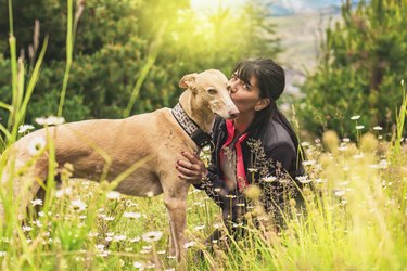 Latin woman kissing her dog outdoors. Sunset sunlight in nature.
