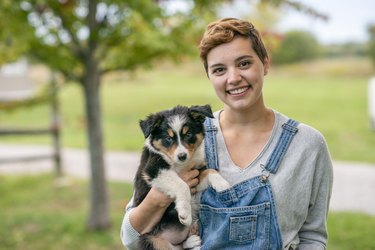 Young woman wearing overalls holding dog outside