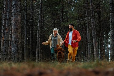 Couple with dog running in forest.