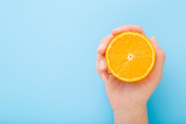 Young woman hand holding half of orange. Fresh fruit. Empty place for text on light blue table background. Pastel color. Closeup. Top down view.