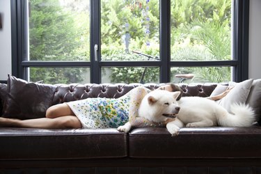young woman lying next to large fluffy white dog on couch